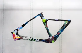 Un cuadro de bicicleta BMC VAR0 colorido con diseño geométrico y el logotipo de BMC cuelga suspendido sobre un fondo claro y liso.