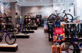 Interior de una tienda de bicicletas con varias bicicletas de carretera Trek BCN Sud en los expositores, accesorios de ciclismo en las estanterías y ropa colgada en los estantes del fondo: tu socio oficial para las aventuras de Gravel Penedès.