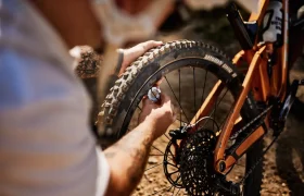 En un entorno exterior soleado, una persona utiliza un manómetro Unior para comprobar la presión de aire del neumático trasero de una bicicleta de montaña.
