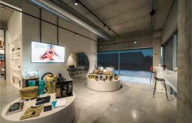 Una moderna tienda de Vic Sports con mesas redondas en las que se exponen aparatos y accesorios, un televisor en la pared, taburetes de bar junto a un mostrador y grandes ventanales por los que entra la luz natural.
