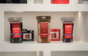 Tres cubiertas de bicicleta Vittoria embaladas se exponen en una estantería blanca, junto a cajas más pequeñas de accesorios de ciclismo de Vic Sports.