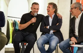Tres hombres sentados en taburetes durante una mesa redonda de Vic Sports; uno de ellos sostiene un micrófono y sonríe, mientras los demás escuchan y ríen.