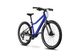La WOOM 4 Explore es una bicicleta azul y negra que cuenta con frenos de disco, un cuadro de acceso bajo y neumáticos con tacos, que se muestran sobre un fondo blanco.