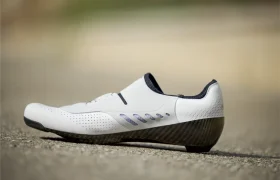 Unas Zapatillas Q36.5 Unique Pro blancas de corte bajo para ciclismo con detalles en negro y suela de fibra de carbono descansan sobre una superficie pavimentada, diseñada para obtener el máximo rendimiento.