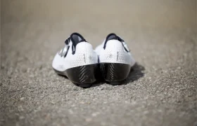 Un par de Zapatillas Q36.5 Unique Pro blancas con suela negra se colocan una al lado de la otra sobre una superficie pavimentada, vistas desde atrás, mostrando su diseño orientado al rendimiento.