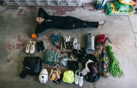 Una persona tumbada en el suelo de un garaje con los brazos detrás de la cabeza, rodeada de material de escalada y de actividades al aire libre perfectamente ordenado: una escena inspirada por el espíritu aventurero de Kilian Jornet y su dedicación a explorar nuevos estados de elevación.